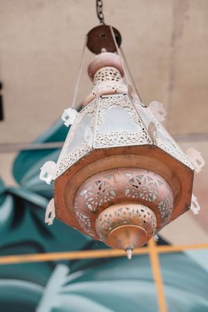 Ornate Moroccan-style copper pendant lantern with intricate cutwork and glass panels hanging against a tropical leaf mural.