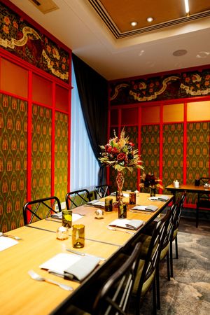 Elegant private dining room with a long wooden table, floral centerpiece, and red-framed green patterned walls.