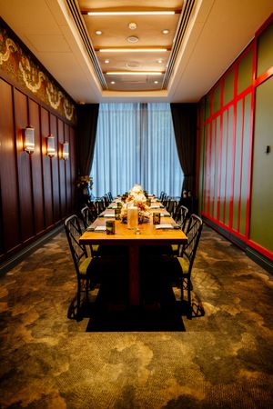 Elegant private dining room with a long set table, black chairs, sheer curtains, wood-paneled walls and warm sconce lighting.
