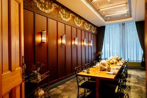 Elegant private dining room with a long wooden table, black chairs, wall sconces, ornate ceiling border, and sheer curtains.