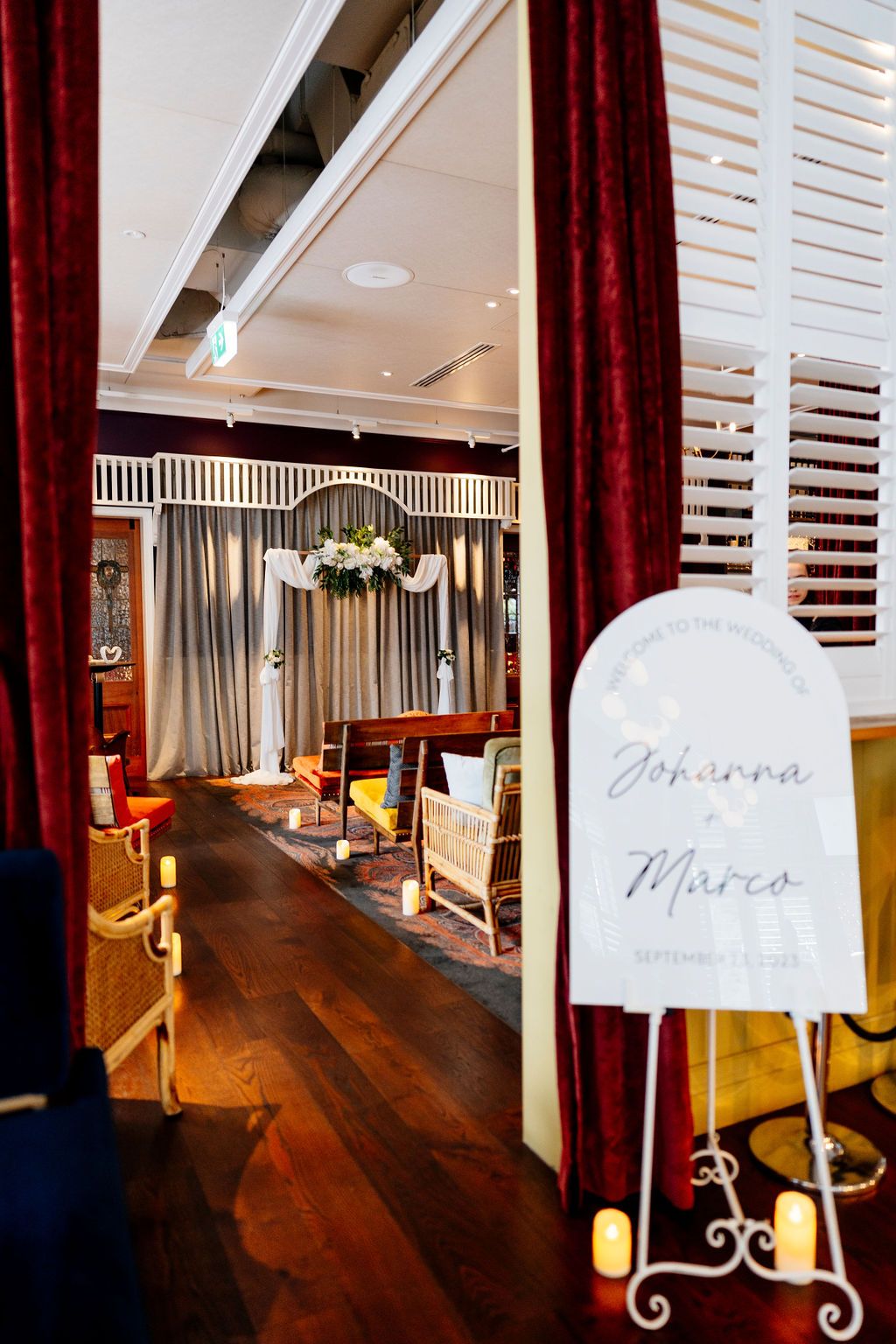 Elegant indoor wedding ceremony space with a welcome sign for Johanna and Marco, floral arch, candles and wooden floors.