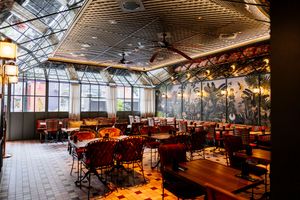 Elegant restaurant interior with red velvet chairs, wooden tables, a glass atrium ceiling, ceiling fans and a tropical botanical mural.