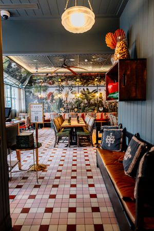 Stylish restaurant interior with red and white checkered tile floor, leather banquette, wooden tables and a tropical botanical mural.