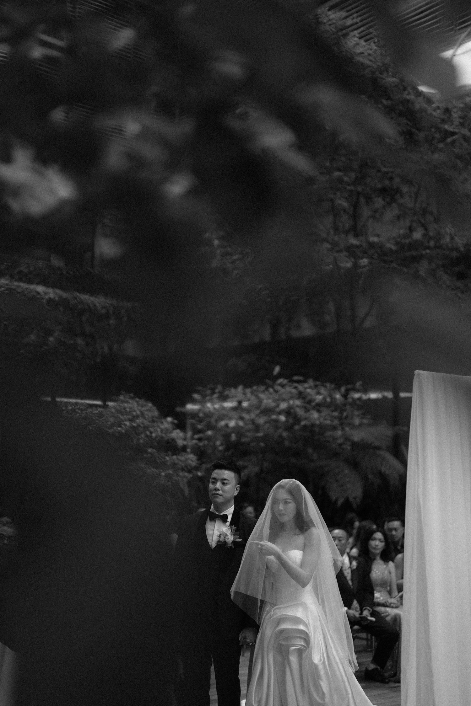 Bride and groom pose elegantly on grand staircase, bride in flowing white gown with long train in ornate venue.
