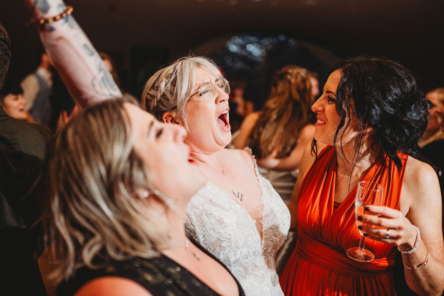 Bride and bridesmaids laughing and dancing joyfully at a lively wedding reception celebration at Oak Tree Farm in Carmarthan