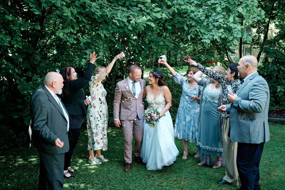 Bride and groom celebrate with guests outdoors under lush green trees at a joyful wedding ceremony.