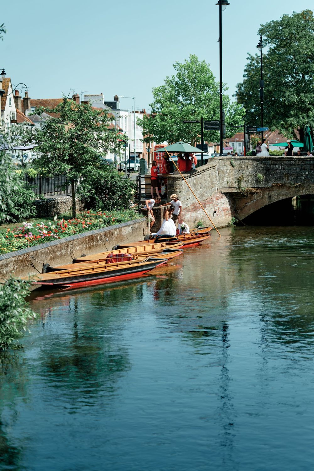Wooden punts moored along a scenic river canal beside a stone bridge in a charming English town on a sunny day.