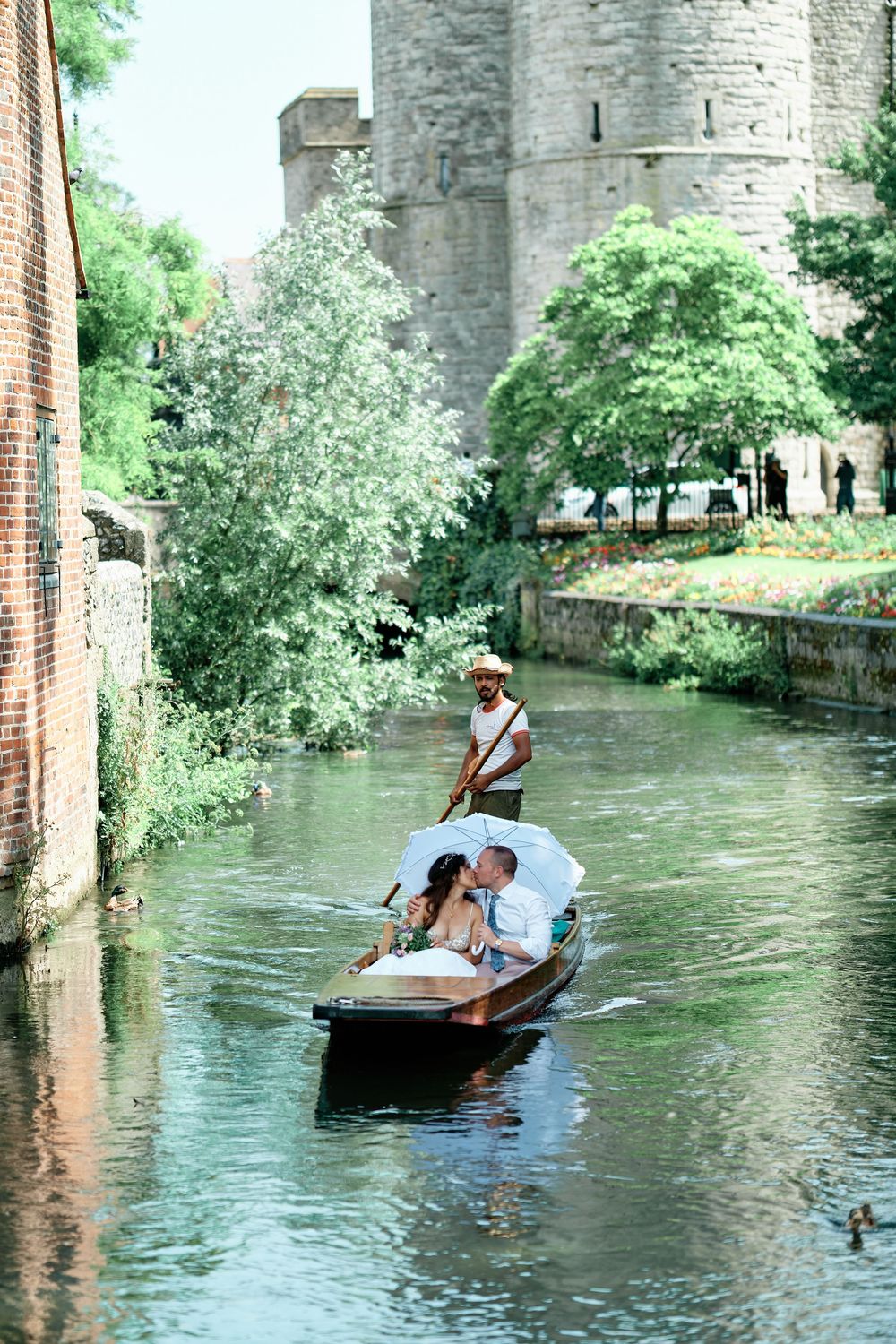 Couple kissing on a romantic punt boat ride along a serene canal beside a historic stone castle.