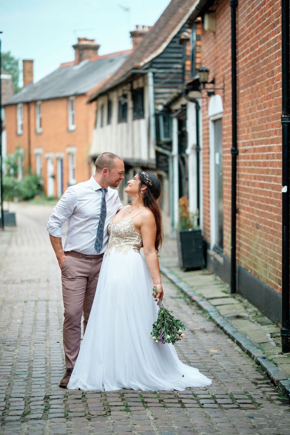 Bride and groom share a romantic moment on a cobblestone street lined with red brick buildings.