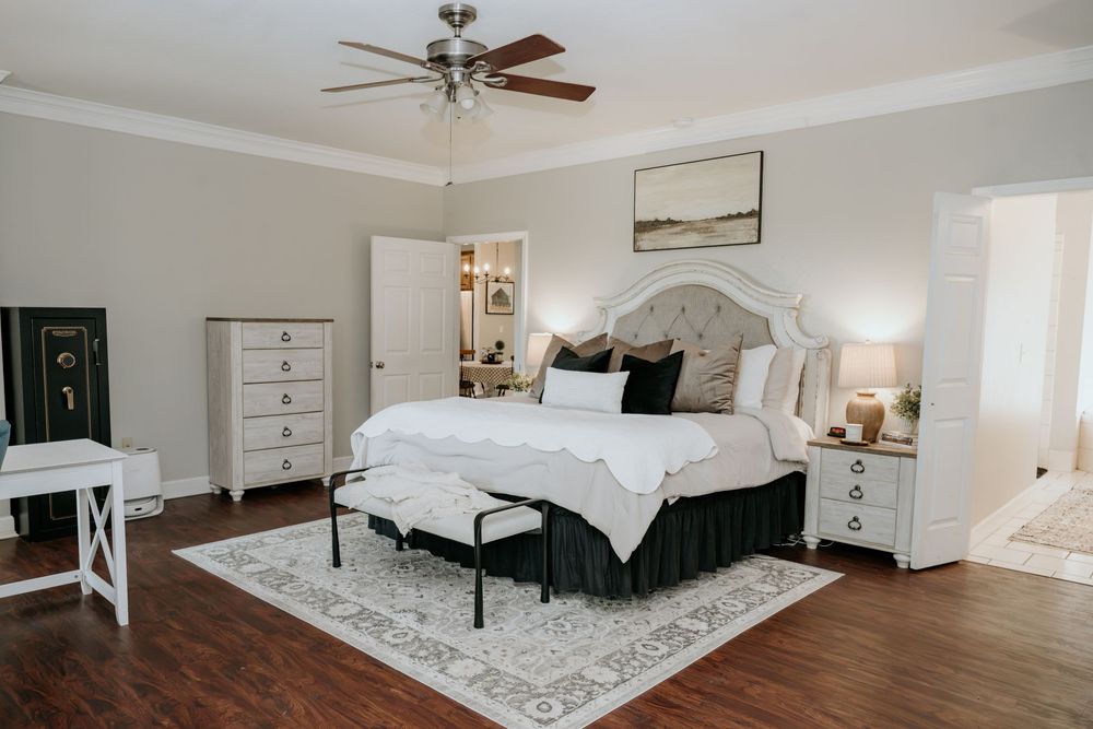 Elegant master bedroom with tufted headboard, hardwood floors, ceiling fan, and classic white furniture accents.