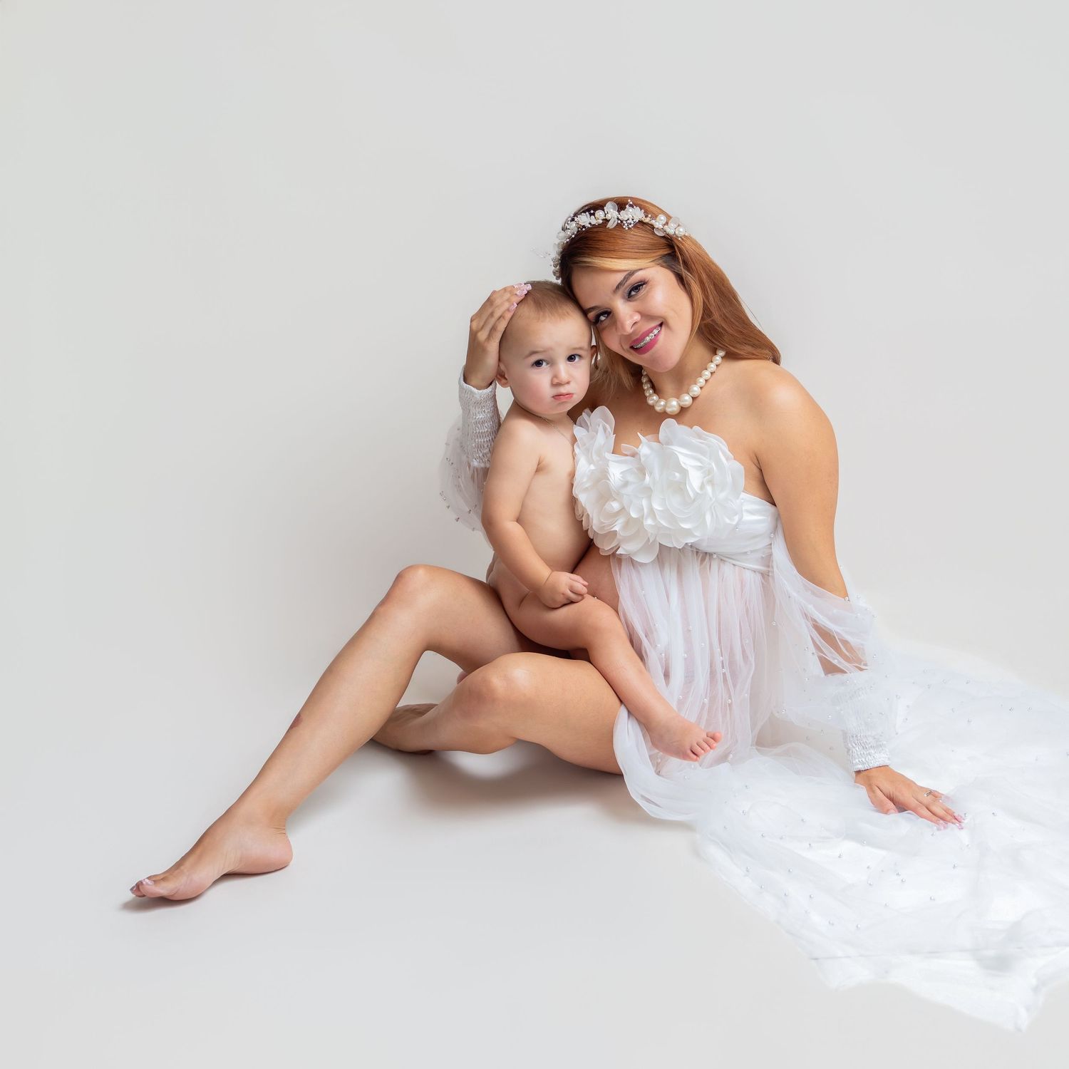 Mother and baby in white angelic outfits posing together in a studio photo shoot.