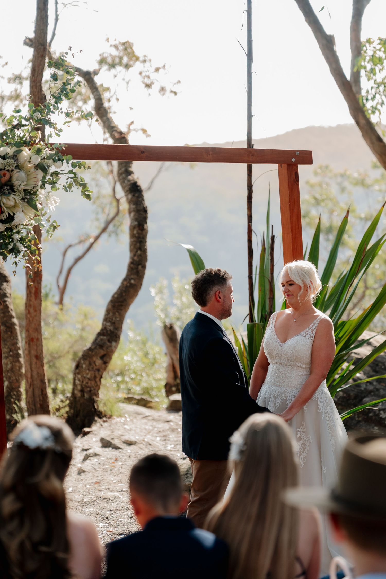 Couple exchanging vows at an outdoor wedding ceremony under a wooden arch with mountain views.
