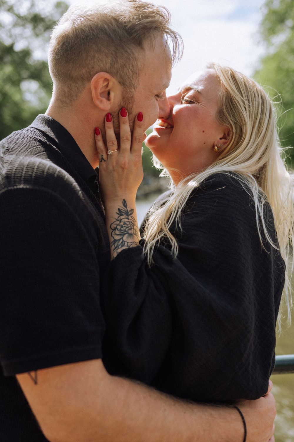 A couple in black outfits sharing a romantic moment outdoors, with the woman tenderly touching the man's face.