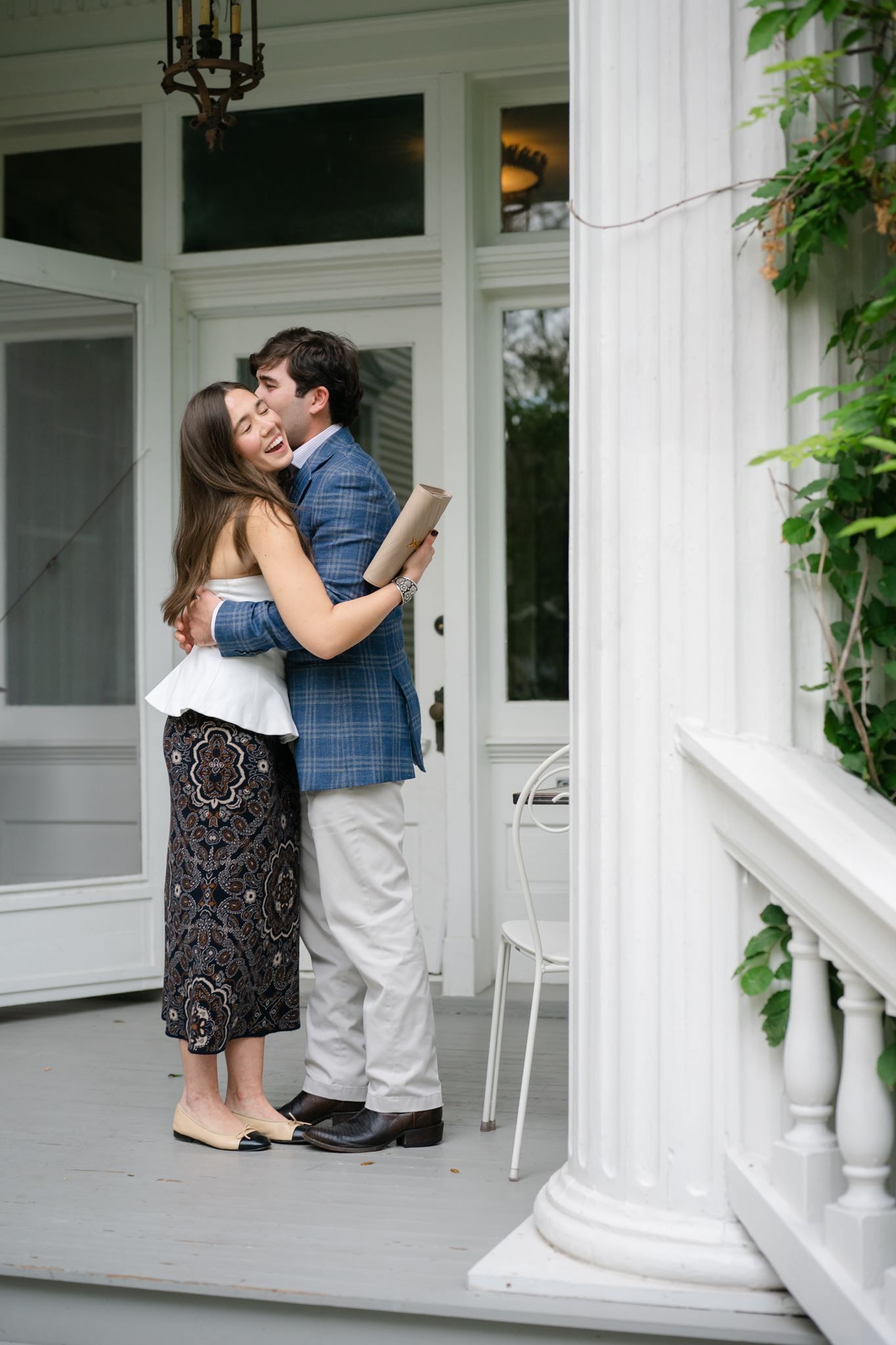 Newly engaged couple hugging while standing on a porch.
