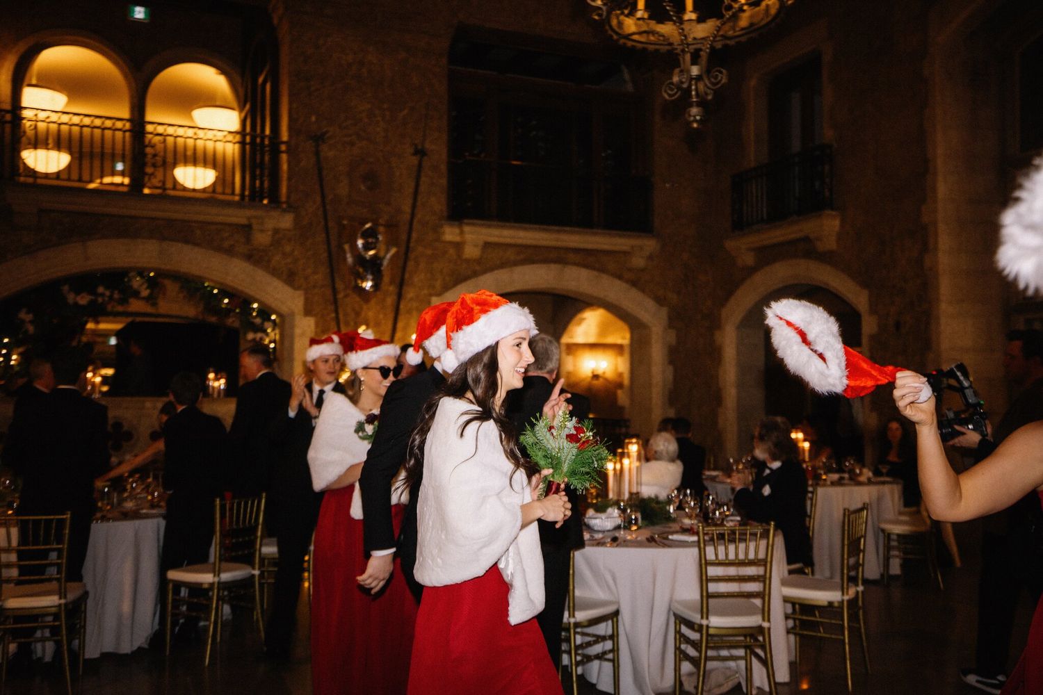 Bridesmaids in Santa hats and red dresses cross the floor as Santa hats wave at a Banff Christmas wedding reception