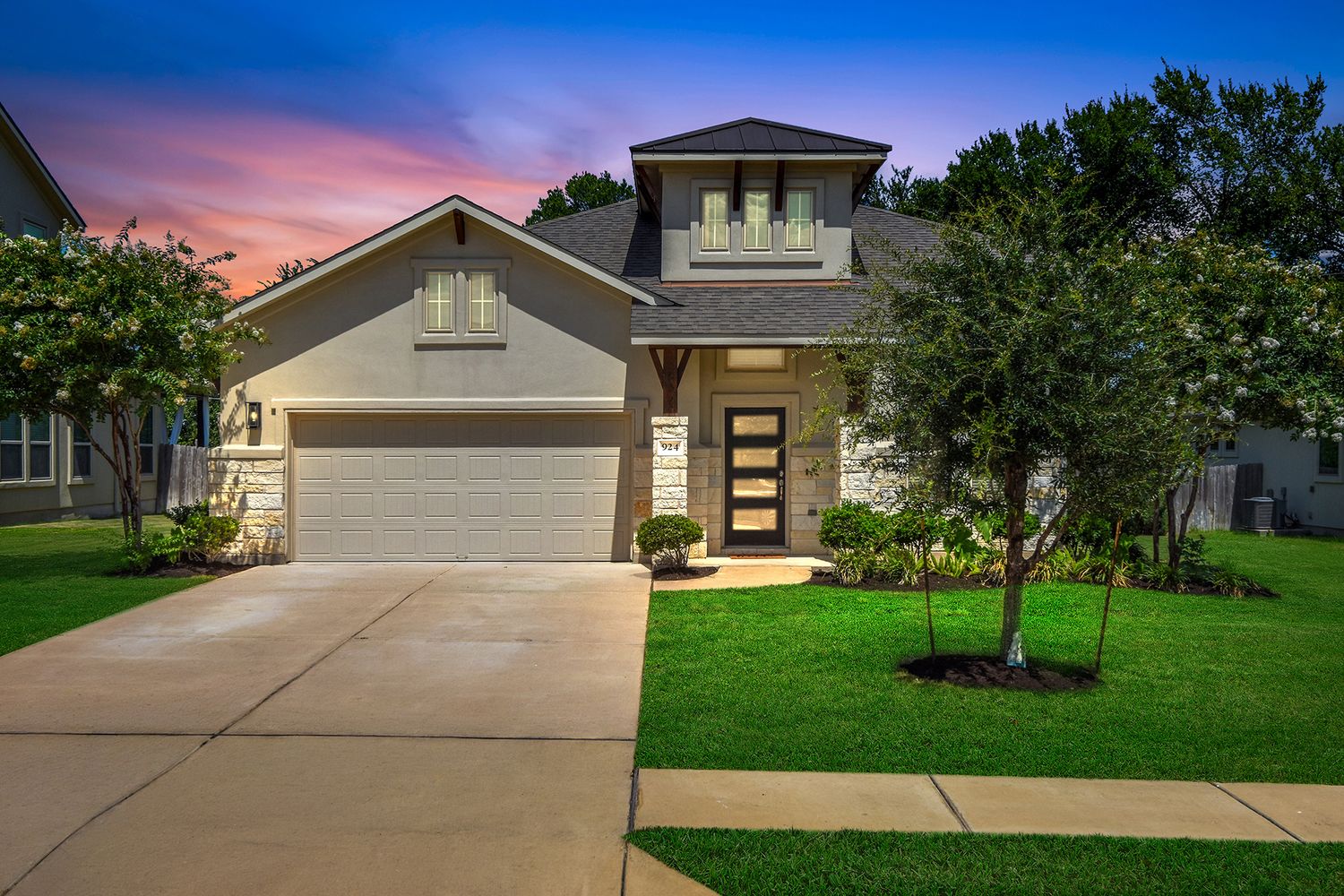 Two-story stone and stucco home with attached two-car garage, landscaped front lawn and mature trees under a virtual twilight sunset sky.