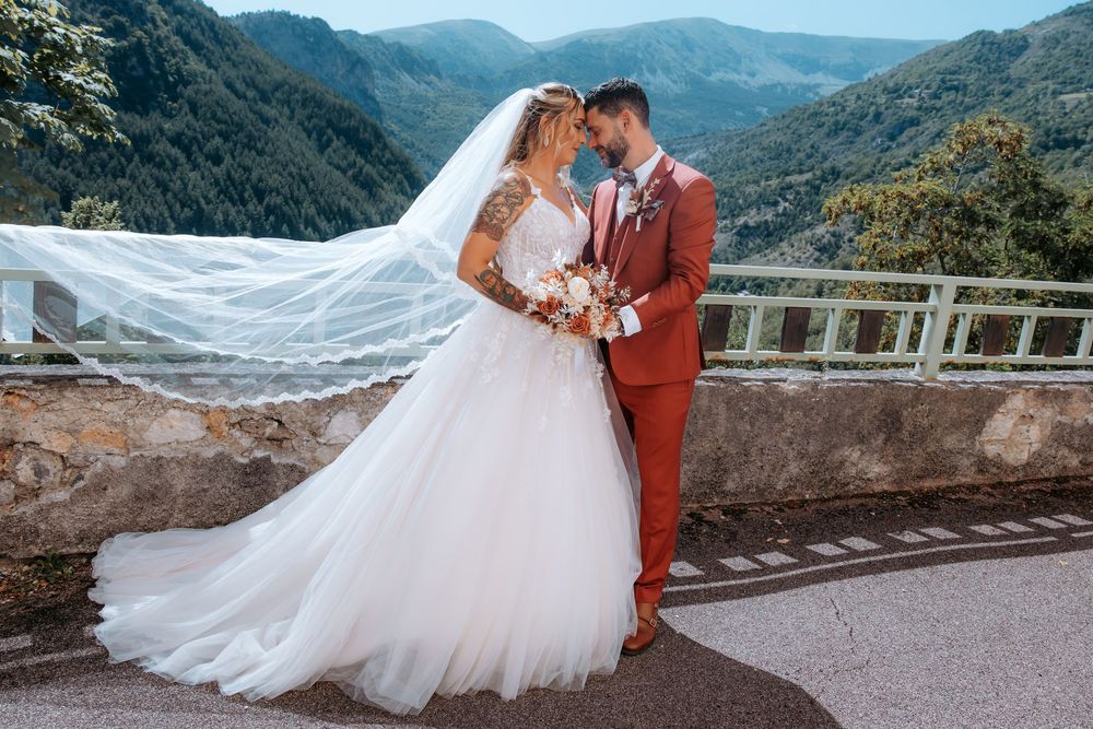 Bride and groom share romantic moment in white gown and rust suit with mountain valley backdrop.