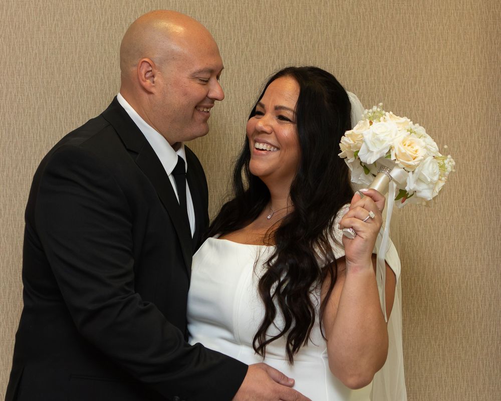 Happy bride and groom smiling together, bride holding white rose bouquet in elegant wedding attire.
