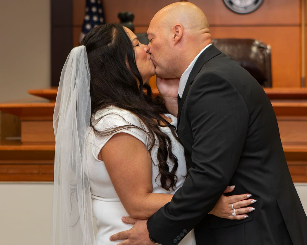 Bride and groom share first kiss at courthouse wedding ceremony, bride wearing white dress and veil.