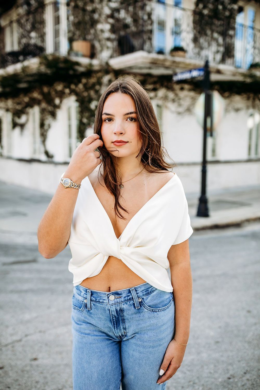 Young woman in white crop top and jeans poses on urban street.