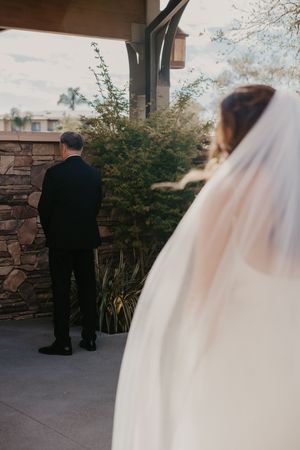 Bride in white veil approaches groom in black suit for wedding first look at elegant stone venue.