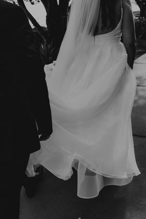 Black and white photo of a bride in a flowing white wedding dress and veil walking with a groom in a dark suit.