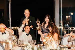 Guests raising glasses in a toast at an elegant wedding reception dinner, dressed in formal attire.