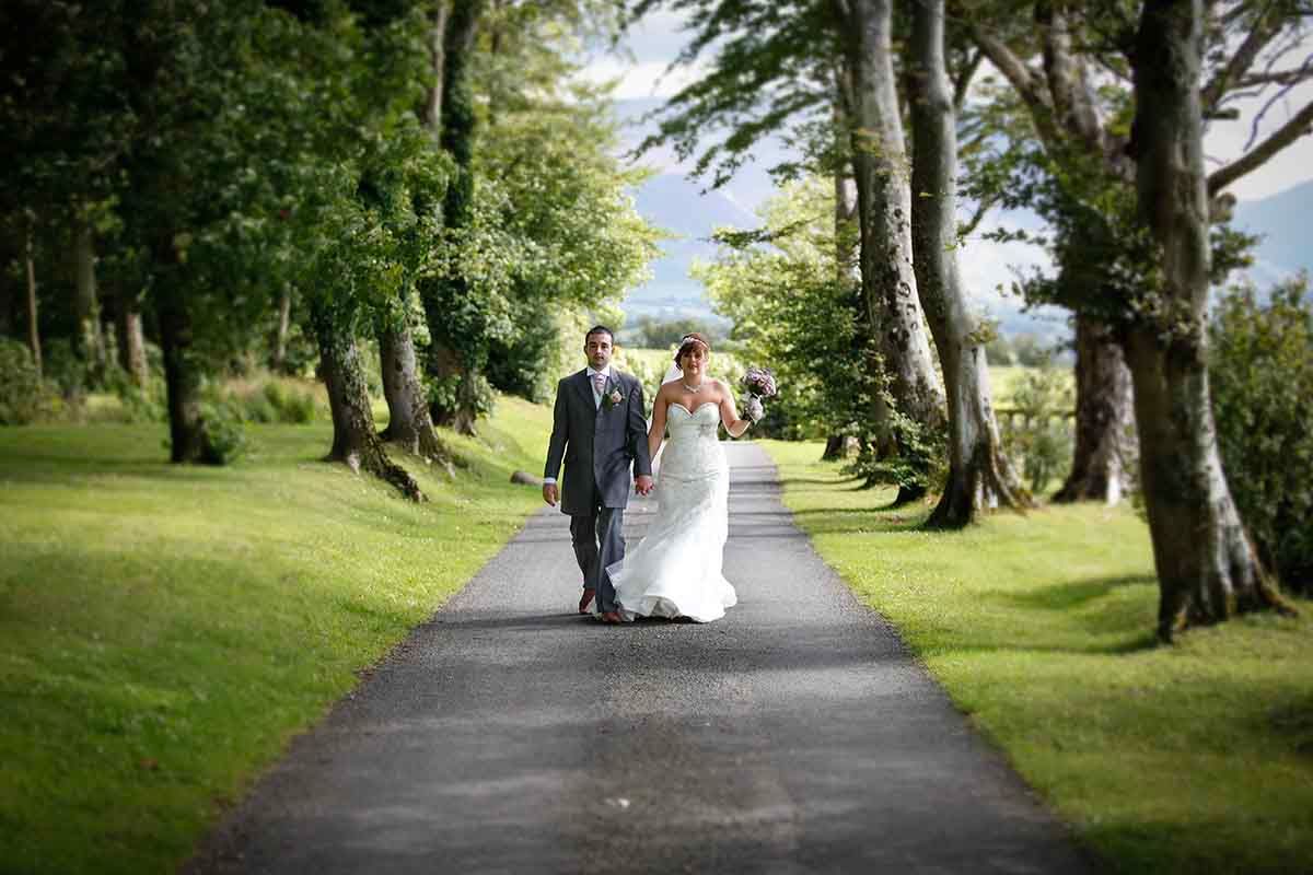 Bride and Groom walk down the tree lined path at Hundith Hill wedding venue near Cockermouth in the Lake District