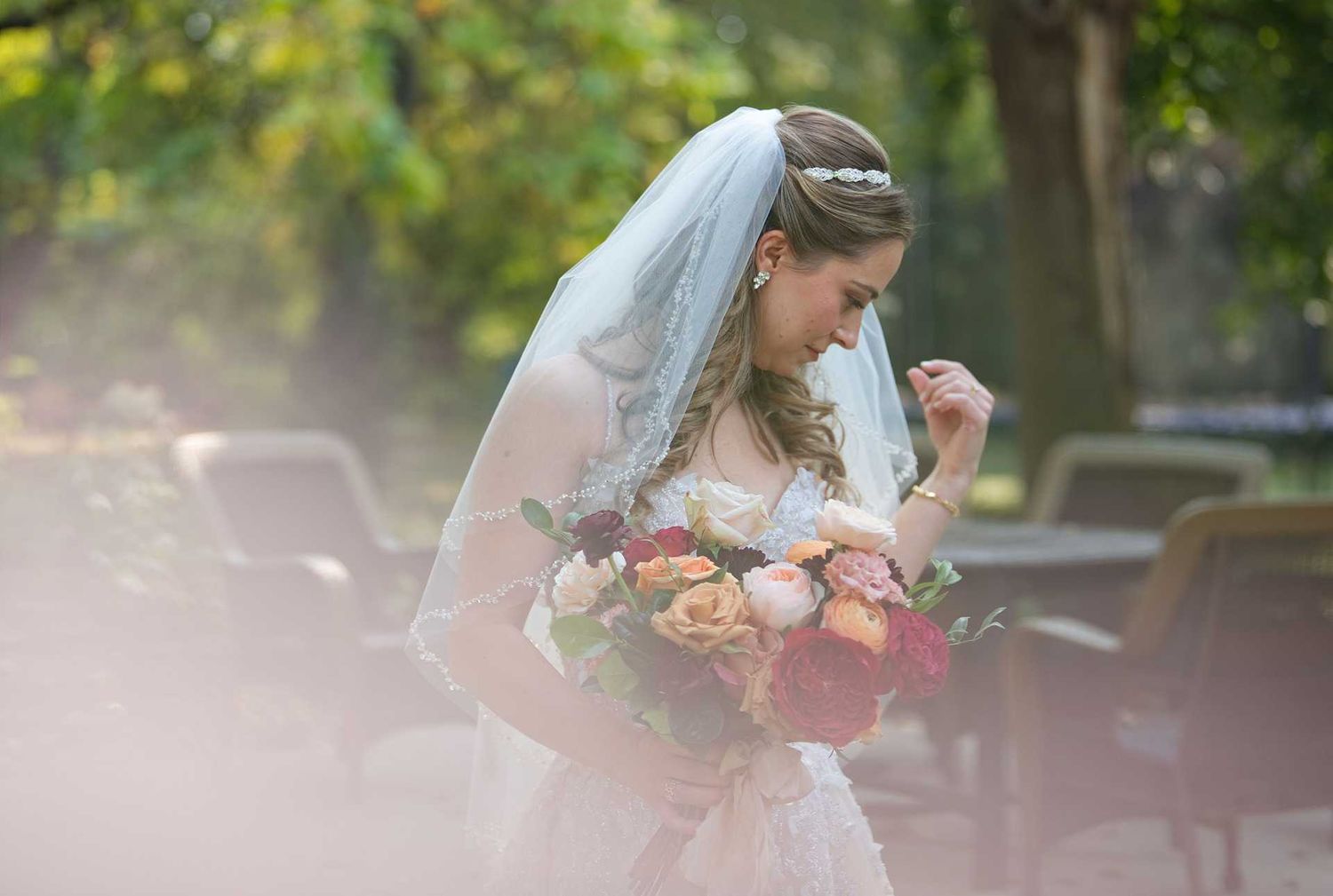 Bride in white wedding dress and veil holding colorful bouquet of flowers outdoors in garden setting.