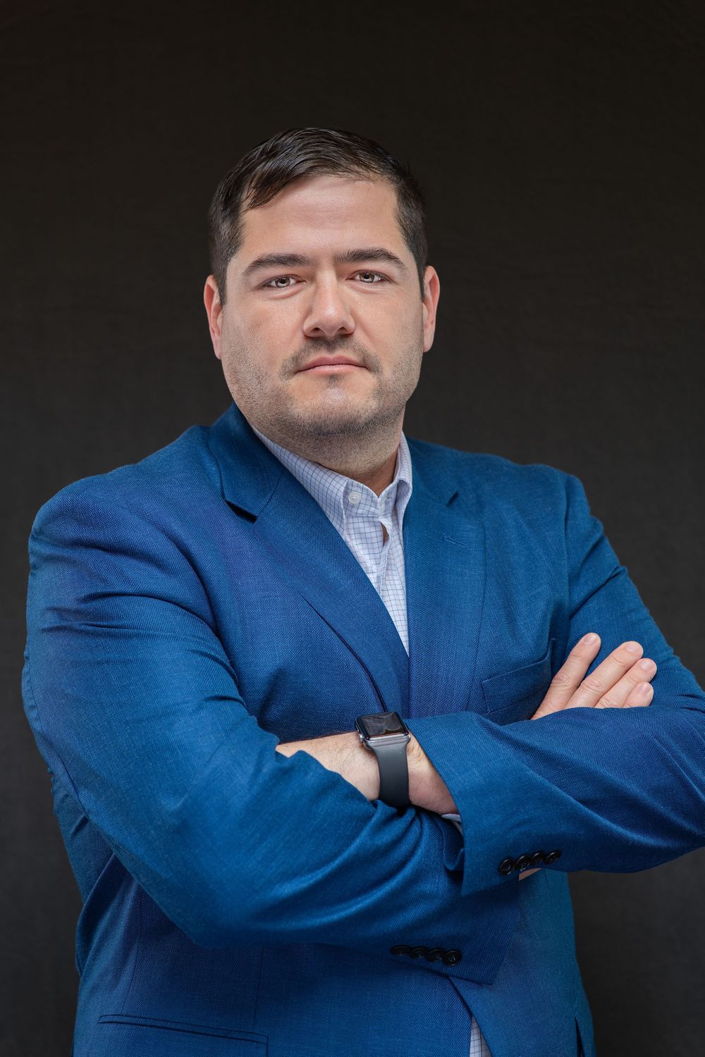 Professional man in blue blazer with arms crossed against dark background, confident business portrait.