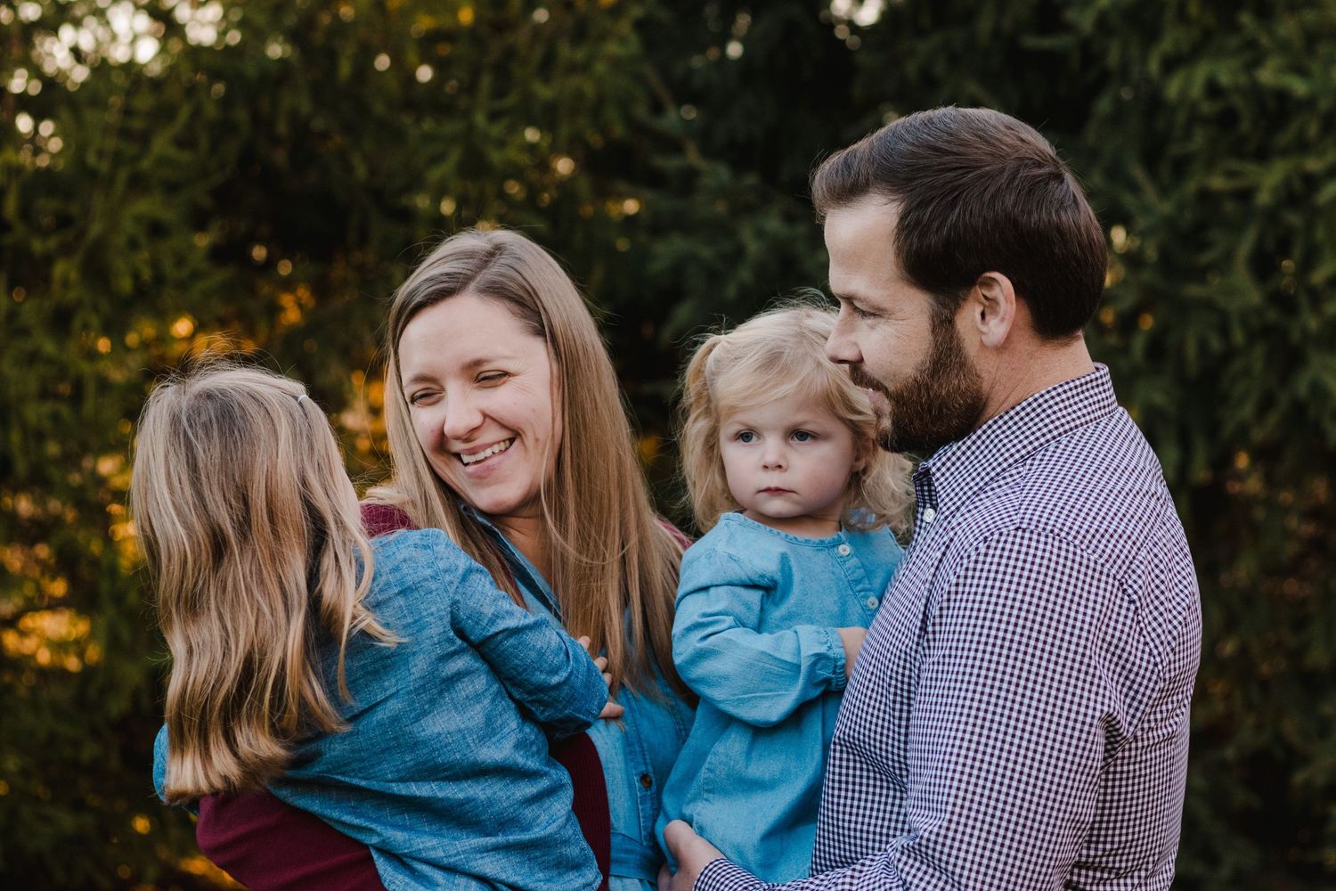 A happy family of four enjoys a warm outdoor moment, with two young children in denim jackets and parents smiling.