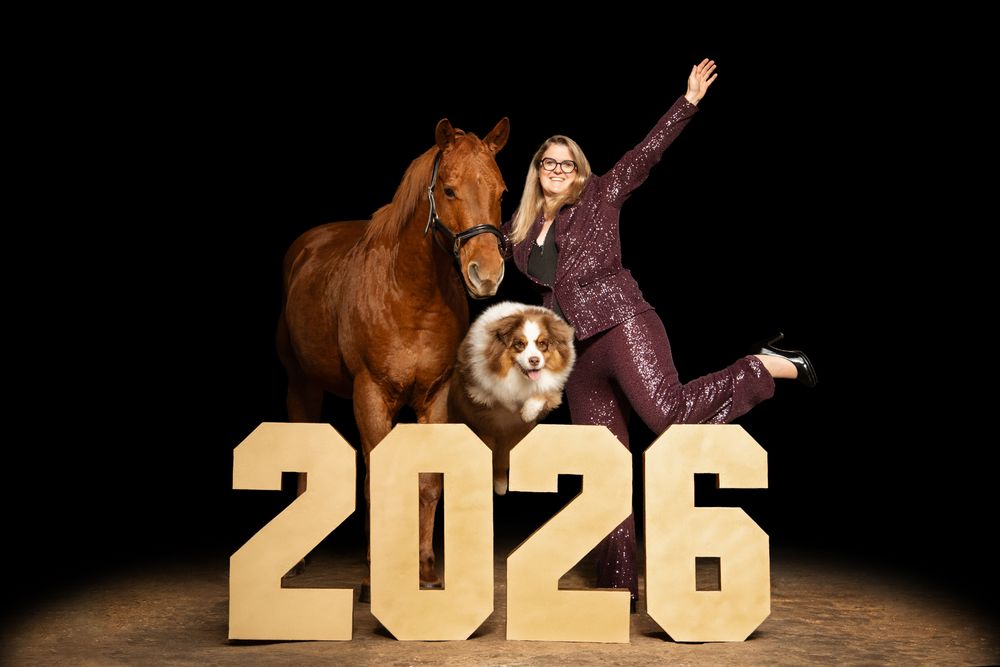 Woman posing with a chestnut horse and Australian Shepherd dog beside gold 2026 numbers on a dark background.