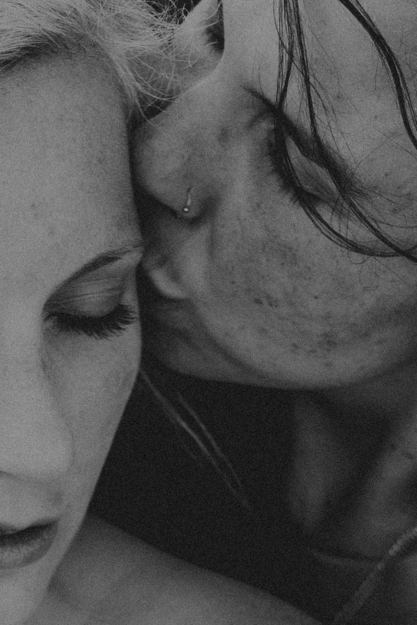 Black and white close-up of two people sharing an intimate moment, foreheads nearly touching, eyes closed.