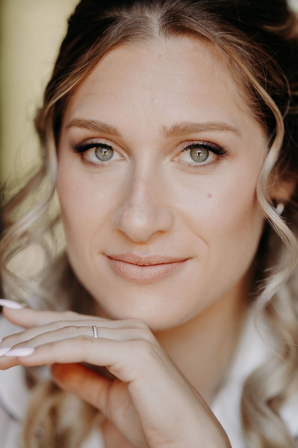 Close-up portrait of a blonde woman with green eyes wearing natural makeup and a diamond ring.