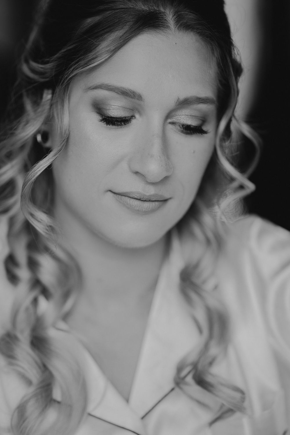 Black and white close-up portrait of bride with curly hair and glamorous wedding makeup.
