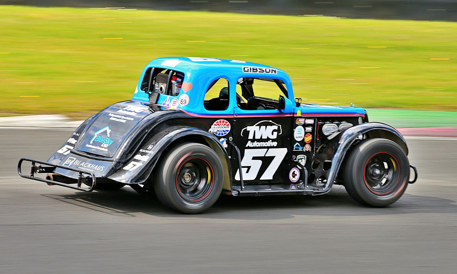 Vintage-style number 57 TWC Automotive legend car racing on a motorsport circuit.