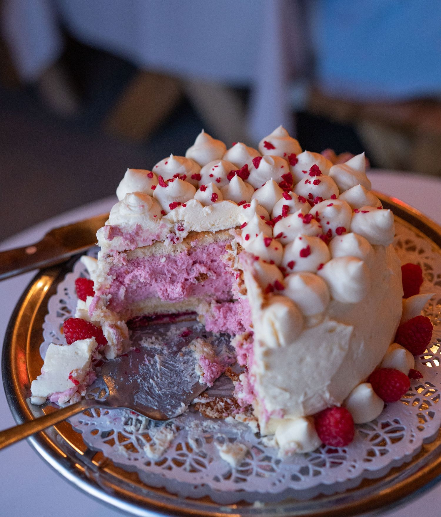 Elegant raspberry layer cake with meringue topping and fresh berries on a decorative doily plate.