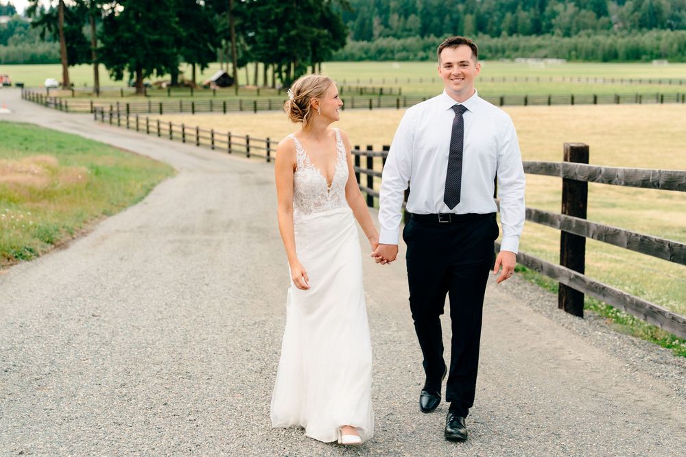 Bride and groom holding hands walking down a scenic country road lined with wooden fences.