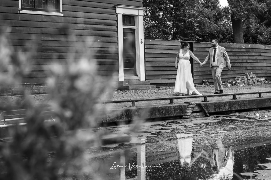 zwart wit foto, bruidspaar loopt langs een slootje in zaandam, reflectie in het water