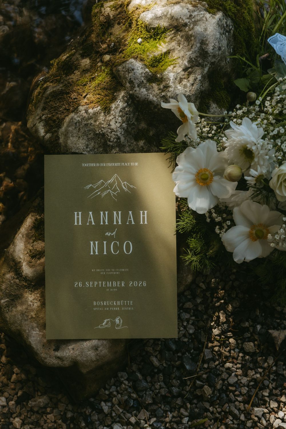 Olive green wedding invitation for Hannah and Nico on September 26 2026 beside white flowers on moss.