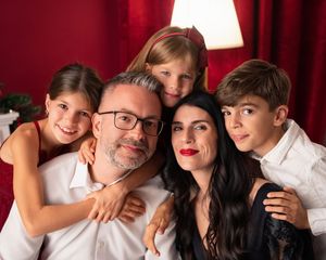 Happy family of five posing together against a red background, parents with three children smiling warmly.