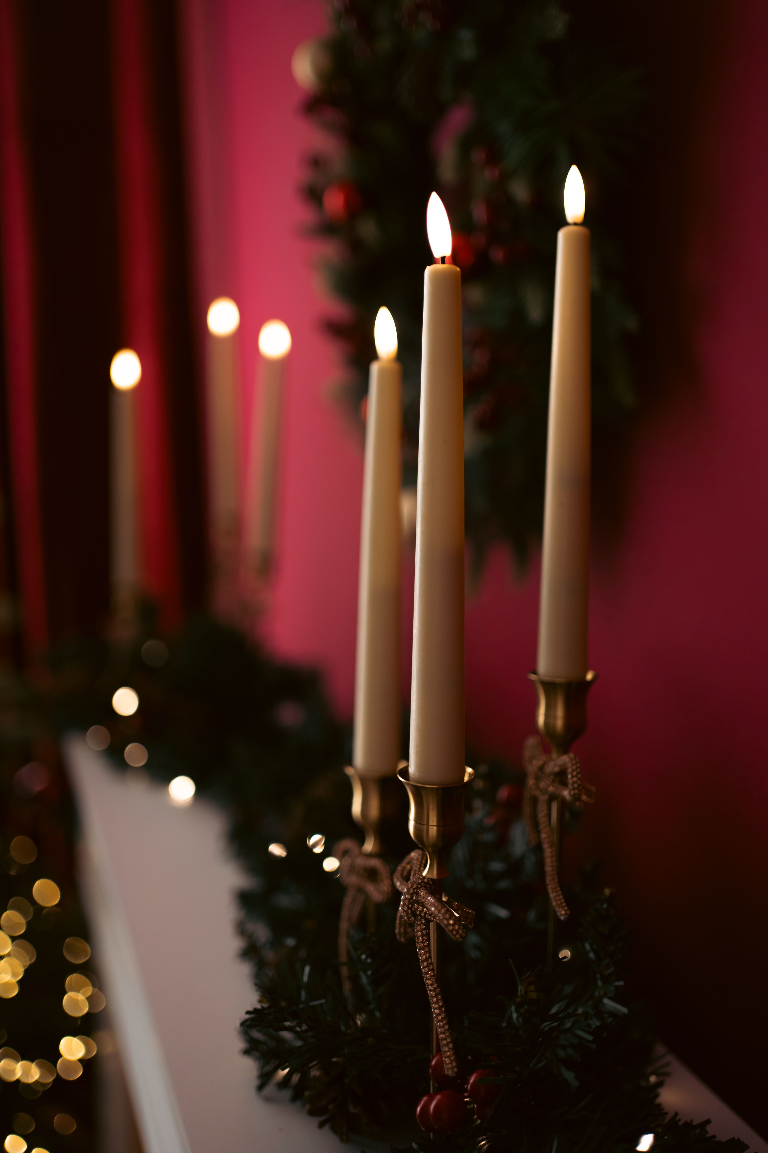 Elegant brass candelabra with lit taper candles on a Christmas garland mantle against a rich red wall.
