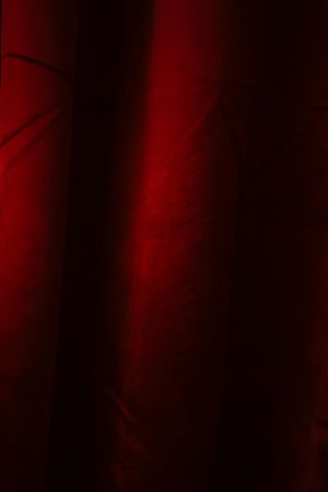 Deep red velvet curtains with dramatic lighting creating rich, dark shadows and elegant folds of fabric.