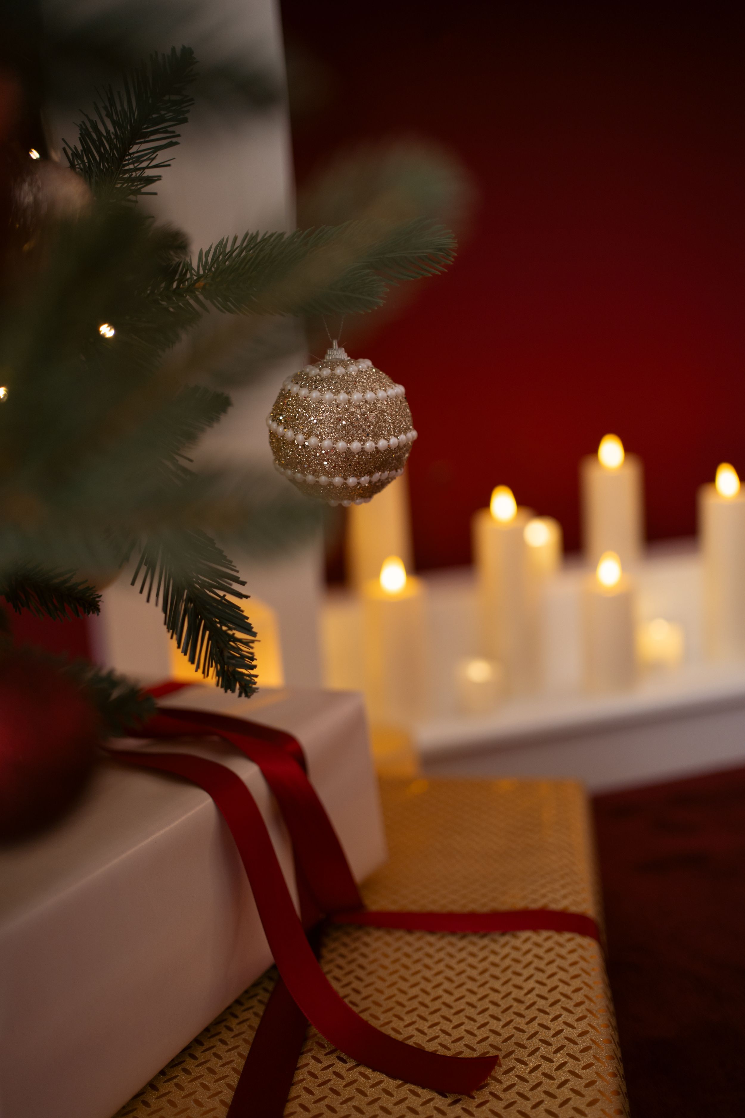 Christmas tree with ornament and gift beside glowing candles on red background.