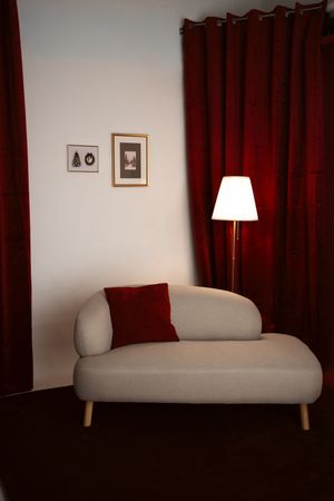 Cozy living room corner with a cream chaise lounge, red velvet curtains, floor lamp, and framed wall art.