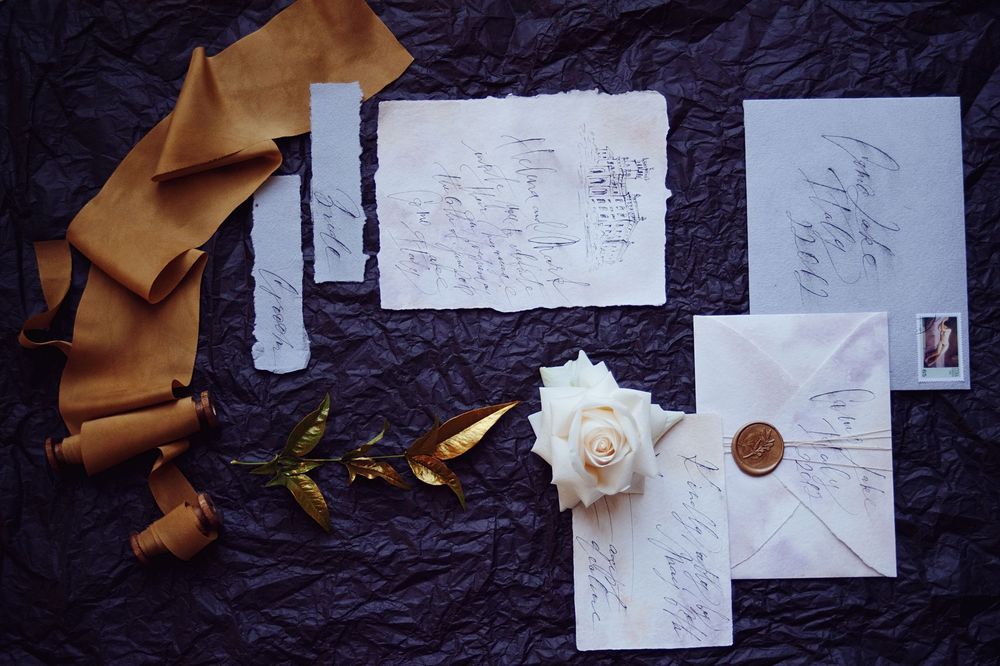 Flat lay of elegant wedding stationery with calligraphy, wax seal envelope, white rose, and ribbon.