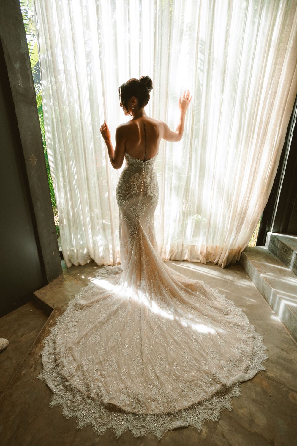 Dramatic moody picture of bride showing off back of dress by the window in Tulum Mexico