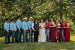 Wedding party poses outdoors in cowboy attire, groomsmen in blue shirts and bridesmaids in red dresses.