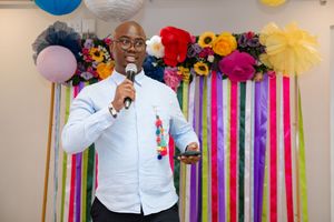 Event speaker addressing guests in front of the vibrant floral and ribbon backdrop.