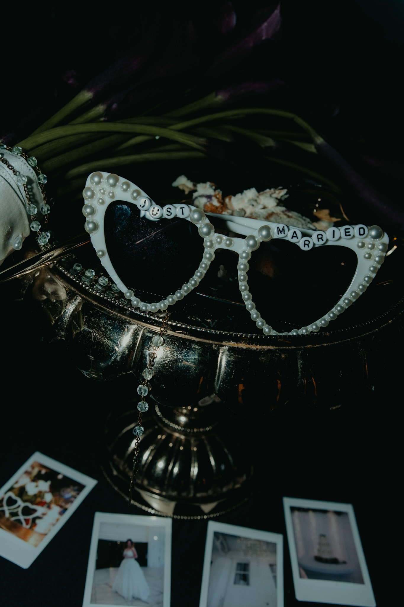 Heart-shaped "Just Married" pearl sunglasses displayed on a silver stand with Polaroid photos nearby.